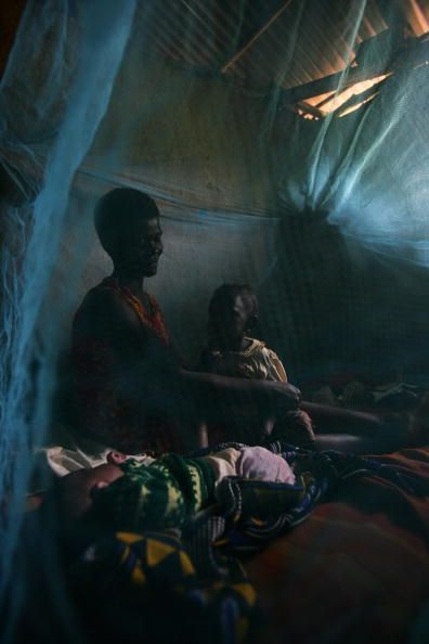 Une mère et son enfant assis sous une moustiquaire imprégnée d'insecticide qui permet d'arrêter les moustiques porteurs du paludisme.